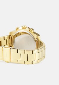 Gullfarget klokke med metalarmbånd, kronograffunksjoner og rund kasse. Klart glassur viser klokkeviseren.