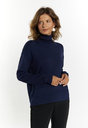 Maglione a dolcevita blu navy in un morbido tessuto lavorato. Presenta spalle scese e polsini a costine, abbinato a pantaloni neri.