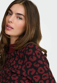 Pull noir avec un imprimé léopard rouge, manches longues et col rond. Le tissu semble doux avec une finition texturée.