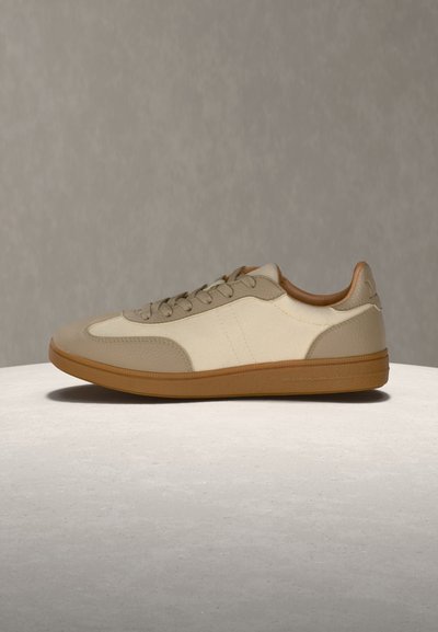 Χαμηλού προφίλ καθημερινό αθλητικό παπούτσι σε μπεζ και κρεμ με ταμπά λαστιχένια σόλα, κλείσιμο με κορδόνια και επένδυση στο γιακά, παρουσιασμένο σε στρογγυλή επιφάνεια.