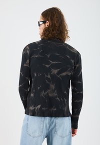 Sort ribbet langærmet beklædningsgenstand med et tie-dye mønster i lysere nuancer, designet med en afslappet pasform og lige kant.