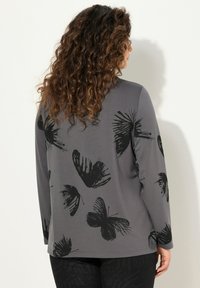 Maglia grigia a maniche lunghe con stampa di farfalla nera. Il tessuto ha una consistenza liscia e una vestibilità comoda, con un orlo arrotondato.