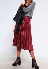 Karmosinfärgad plisserad midi kjol, glänsande satintyg, kombinerad med en grå topp och svart läderjacka. Klumpiga svarta klackar med mesh-strumpor.