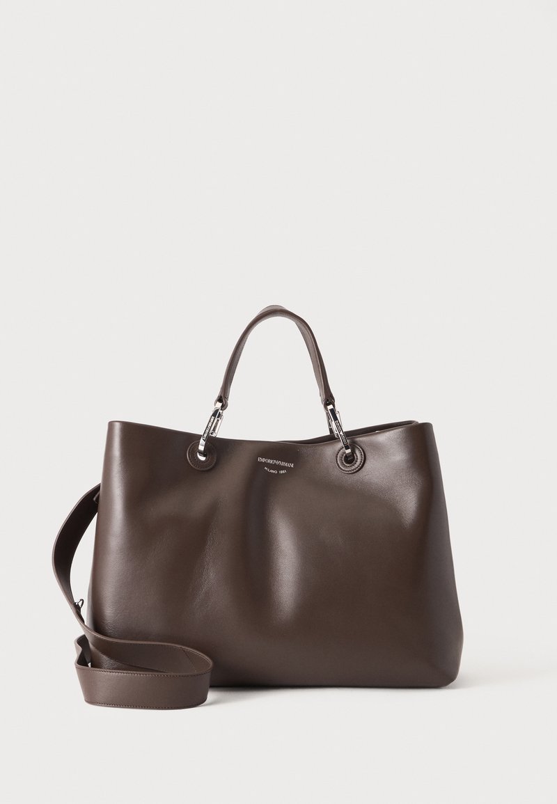 Sac à main en cuir marron foncé avec deux petites poignées, une longue bandoulière réglable et des détails en métal argenté sur un fond uni.