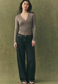 Lange mouw, V-hals top in taupe, gecombineerd met hoge taille, wijde zwarte jeans. Platte sandalen en een minimalistisch ontwerp.
