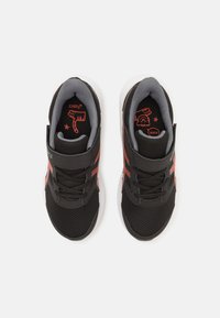 Black athletic shoes with gray mesh upper and white soles. Features a velcro strap, textured fabric, and red graphic accents inside.