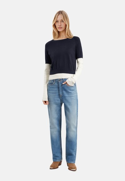 Maglione corto blu navy e crema con scollatura rotonda, abbinato a jeans a gamba dritta azzurri chiari e stivali con tacco marroni.