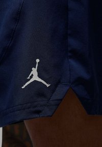 Marineblå atletiske shorts med ventileret søm og et hvidt Jumpman-logo nederst til venstre, lavet af et glat, let materiale.