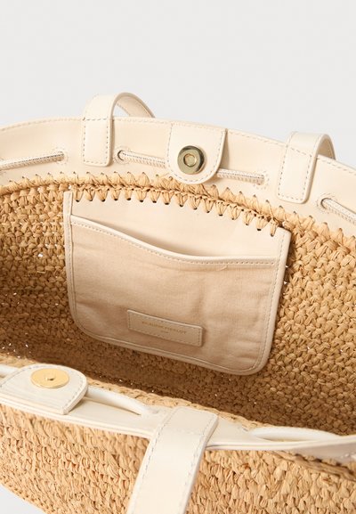Μπεζ υφαντή τσάντα από ψάθα με λευκή δερμάτινη διακόσμηση, εσωτερική μπεζ υφασμάτινη τσέπη και χρυσό μαγνητικό κούμπωμα.