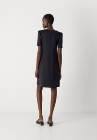 Robe à manches courtes, de couleur bleu marine foncé, avec une silhouette droite, un détail de manches bouffantes discrètes et une fermeture éclair au dos, fabriquée en tissu lisse.