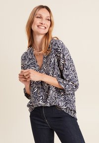 Marinebluse mit weißem Blattmuster, V-Ausschnitt und Dreiviertelärmeln, kombiniert mit dunklen Jeans. Weicher Stoff und lässige Passform.