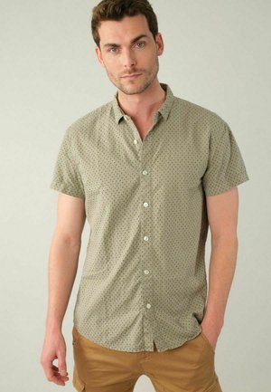 Chemise à manches courtes à boutons en vert olive clair, avec un motif à pois, un col classique et une coupe décontractée. Tissu lisse et teintes neutres.
