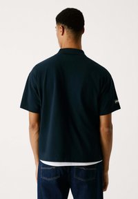 Mörkblå piké med kort ärm och krage. Denna skjorta har en avslappnad passform och är kombinerad med mörkblå denimjeans.