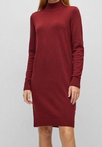 Pletené šaty v barvě burgundy s imitací roláku, dlouhými rukávy, žebrovanými manžetami a lemem. Měkká textura s přiléhavým střihem.