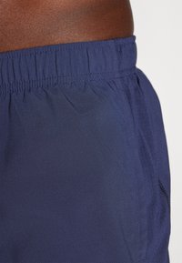Navy blue swim shorts made of lightweight fabric with an elastic waistband and side pockets, featuring smooth texture and minimal stitching.