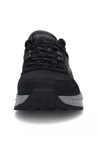 Sneaker nera Skechers con una parte superiore in suede texturizzato e mesh, dotata di un intersuola grigia, punta arrotondata e lacci neri in contrasto.