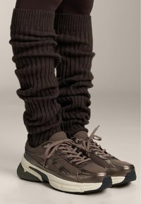 Braune gestrickte Beinwärmer mit Rippenmuster, kombiniert mit braunen und grauen Mesh-Laufschuhen mit gepolsterter Sohle und Schnürsenkeln.