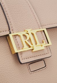 Pink textured leather handbag featuring a gold-tone logo clasp and a black trimmed flap closure. Details include stitching along the edges.