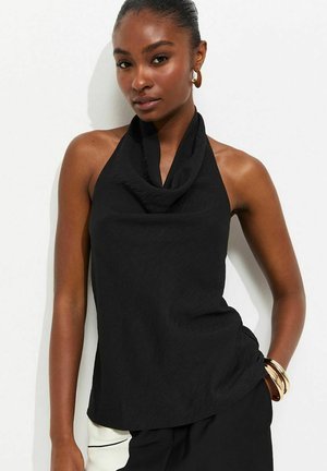 Femme vêtue d'un haut dos nu noir et de boucles d'oreilles anneaux dorés, avec un bracelet doré au poignet sur fond blanc.
