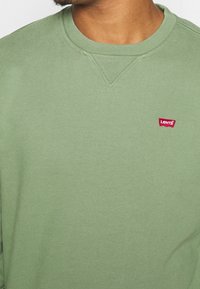 Grön crewneck-tröja av mjukt bomullstyg. Har en liten röd Levi's-logga på bröstet samt ribbade muddar och fåll.