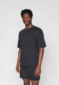 Čierne bavlnené tričko s okrúhlym výstrihom, krátkymi rukávmi a diskrétnym logom potlačeným na hrudi. Spárované s čiernymi šortkami, ktoré ladia.