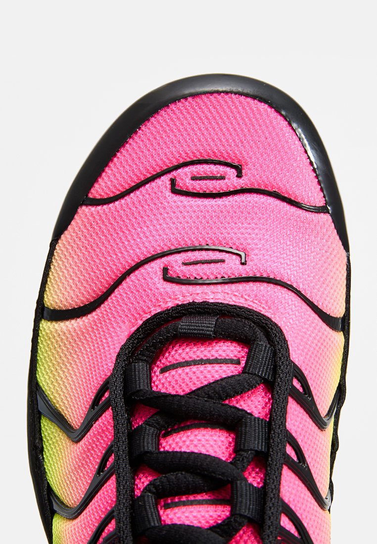 Zapatilla deportiva de malla rosa con detalles y cordones negros, que presenta una superficie texturizada y patrones ondulados en la parte superior. Efecto de color degradado visible.