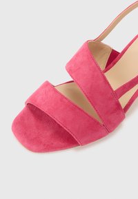 Rosa semsket sandal med brede kryssede stropper, åpen tå, minimal maskinvare og en glatt innersåle. Flat hældesign for komfort.