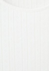 Tissu en tricot blanc avec des côtes verticales et de petits motifs ajourés en forme de diamant.