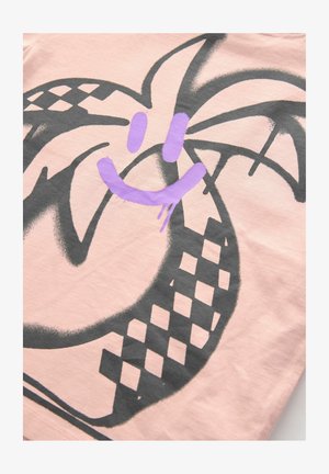 Šviesiai rožinė medvilninė T-shirt marškiniai su dideliu juodu grafiniu piešiniu, kurioje yra stilizuotas šypsena veidas ir delno lapo dizainas, akcentuotas purpurine spalva.