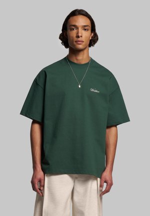 Grünes, übergroßes T-Shirt aus Baumwolle mit Rundhalsausschnitt und kurzen Ärmeln, ausgestattet mit weißem besticktem Text auf der Brust.