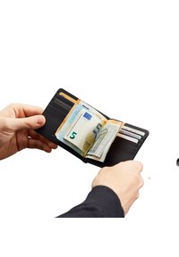 Hände halten eine offene schwarze Brieftasche mit sichtbaren Euro-Banknoten und mehreren Karten in Kartenfächern vor weißem Hintergrund.