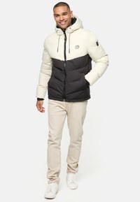 Pudret jakke i kremfarvet og sort med lynlås, hætte og lommer. Bæres over lyse beige bukser og hvide sneakers.