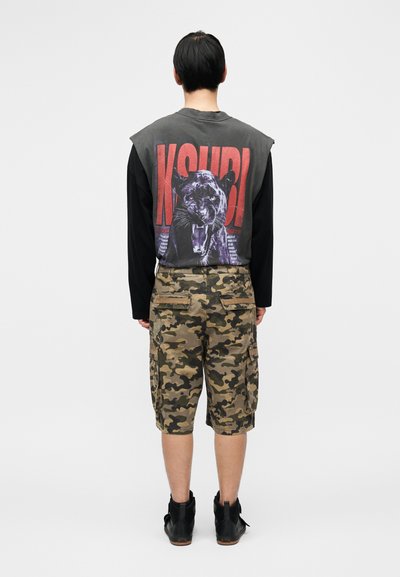 Μαύρο και γκρι γραφικό μπλουζάκι με σχέδιο πάνθηρα και κόκκινο κείμενο, ταιριάζει με παντελόνι cargo καμουφλάζ και μαύρα μποτάκια αστραγάλου.