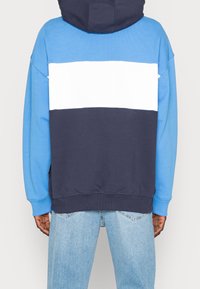 Felpa con cappuccio caratterizzata da un design a blocchi di colore con sezioni blu, bianche e navy. Realizzata in morbido cotone con una vestibilità rilassata.