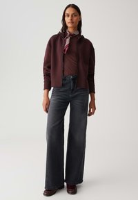 Bordeaux zip-up hoodie over een bruin geribbeld topje, gecombineerd met wijde donkergrijze jeans en bordeauxkleurige schoenen, gestyled met een gestreepte sjaal.