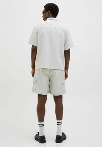 Chemise à manches courtes gris clair avec une finition texturée, accompagnée de shorts cargo gris clair dotés de deux poches latérales et de chaussures noires.