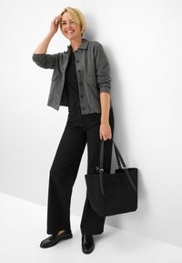 Giacca grigia a bottoni con due tasche davanti, abbinata a un top nero e pantaloni neri a gamba larga. Tiene una borsa tote in suede nera. Mokasini neri.