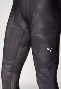 Fekete sport leggings, diszkrét terepmintával, rugalmas anyagból készült, testhez simuló fazonnal. Kis fehér logót tartalmaz.