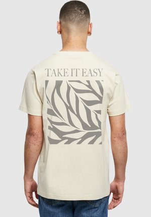 Krém színű pamut póló, szürke levélmintával és a hátoldalán a "TAKE IT EASY" felirattal. Klasszikus, kerek nyakú kivitel.
