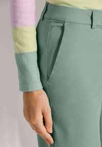 Groene katoenen broek met zijzakken, gecombineerd met een veelkleurige gestreepte trui in roze, geel en lichtblauwe tinten.