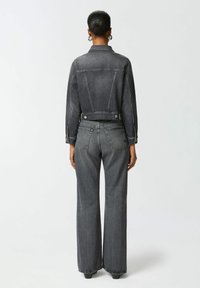 Tamno sivi traper jakna s krojenjem na kraćem dizajnu, istaknutim šavovima i kopčanjem na dugmad. Uparena s tamno sivim trapericama širokih nogavica koje imaju stražnje džepove.