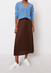 Hellblauer Cardigan mit V-Ausschnitt und drei Knöpfen, kombiniert mit einem braunen, plissierten Maxikleid und weißen Sneakers mit beigen Akzenten.