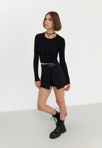 Haut noir à manches longues côtelé associé à une mini-jupe noire enroulée avec une boucle circulaire. La tenue est complétée par des bottes noires à lacets.