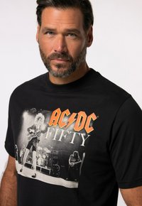 Černé bavlněné tričko s grafickým potiskem rockové skupiny AC/DC a textem "FIFTY" v oranžové barvě, s měkkou texture a klasickým designem s kulatým výstřihem.
