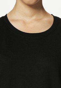 T-shirt en coton noir avec un col rond, une texture lisse et des détails de couture minimalistes autour du col.