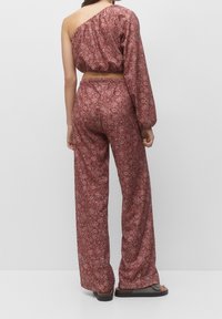 Ensemble deux pièces comprenant un crop top asymétrique à une épaule et un pantalon à jambes larges, en tissu bordeaux avec des motifs floraux détaillés.