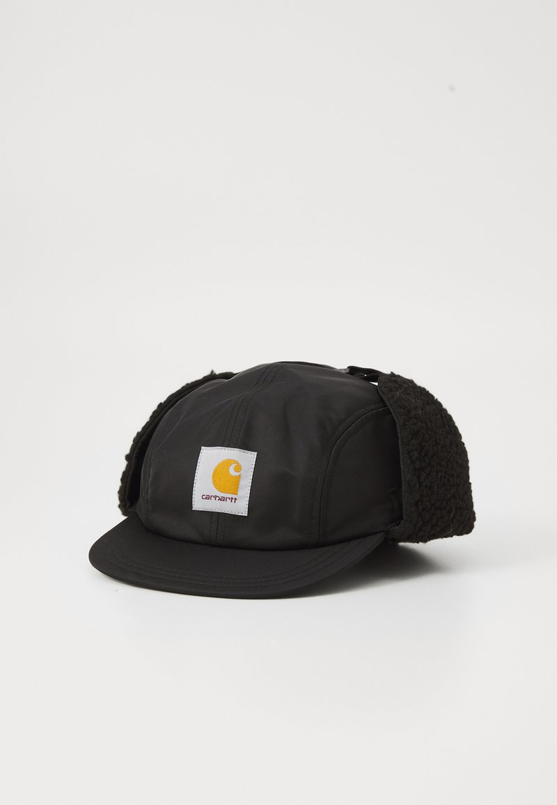 Čierna čiapka s jemným, plyšovým dizajnom uší, žltou nášivkou loga Carhartt a zakriveným brímom. Nepremokavý materiál s matným povrchom.