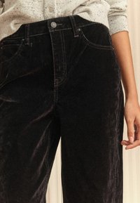 Zwarte corduroy broek met een hoge taille, zichtbare stiksels en voorzakken. Voorzien van een knoop- en haaksluiting bij de taille.