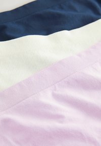 Drie stofstalen in marineblauw, crème en lichtroze. Elk segment heeft gladde en geribbelde texturen, met subtiele kleurovergangen.