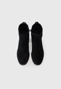 Botines de ante negro con punta redonda y cremallera lateral. Las suelas son planas y el interior está forrado con un tejido suave.